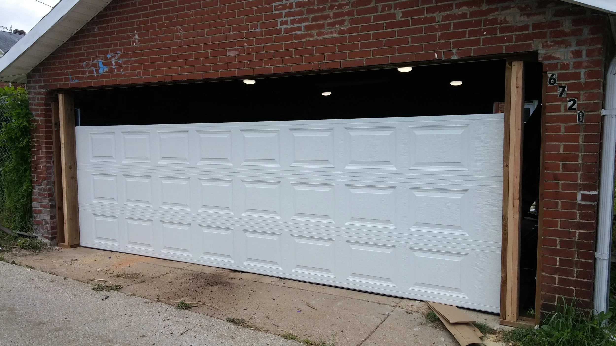 Brick garage with most of the new white sectional door installed, final panels remaining