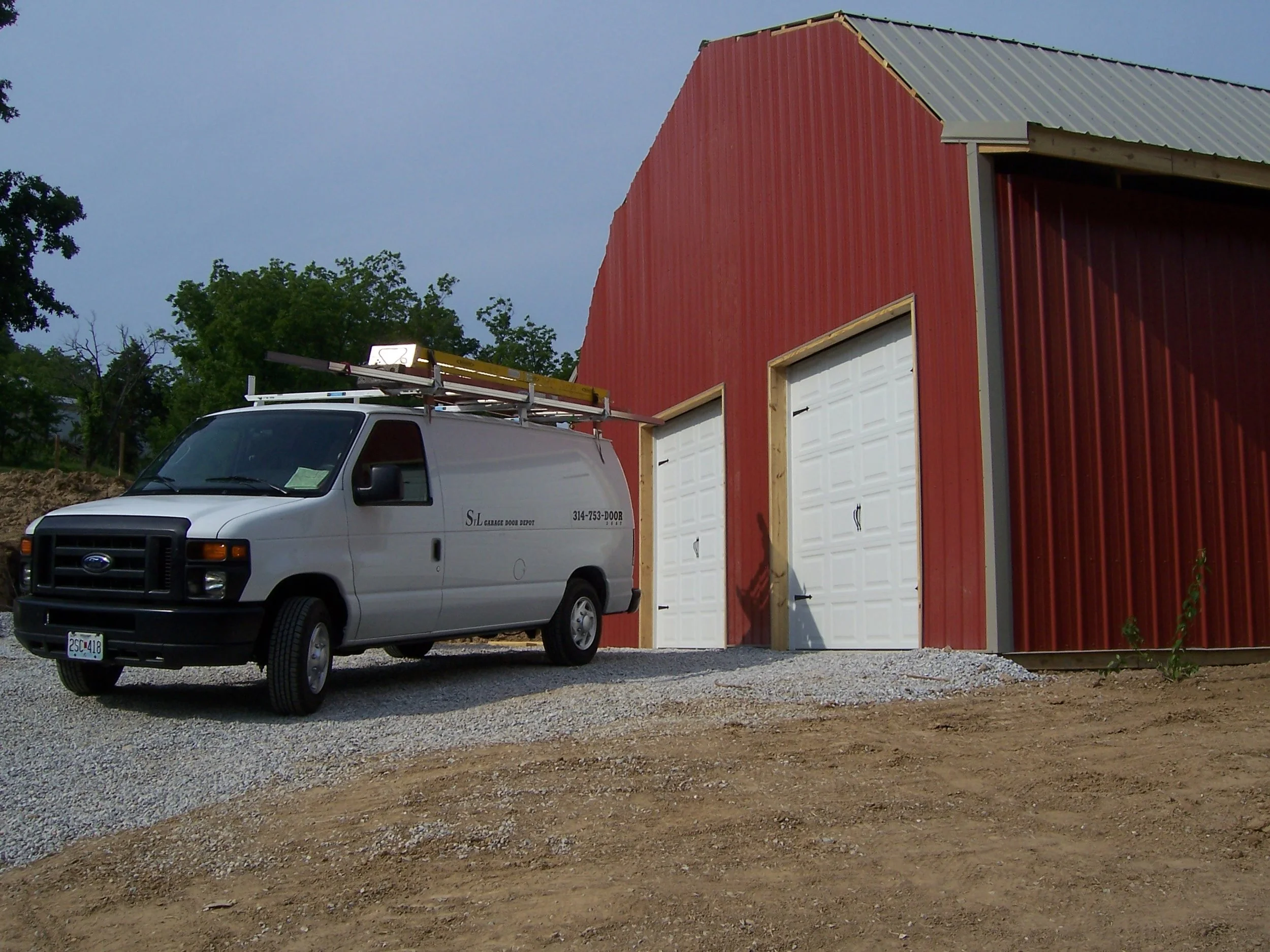 Service van parked next to a red metal building with two new white garage doors