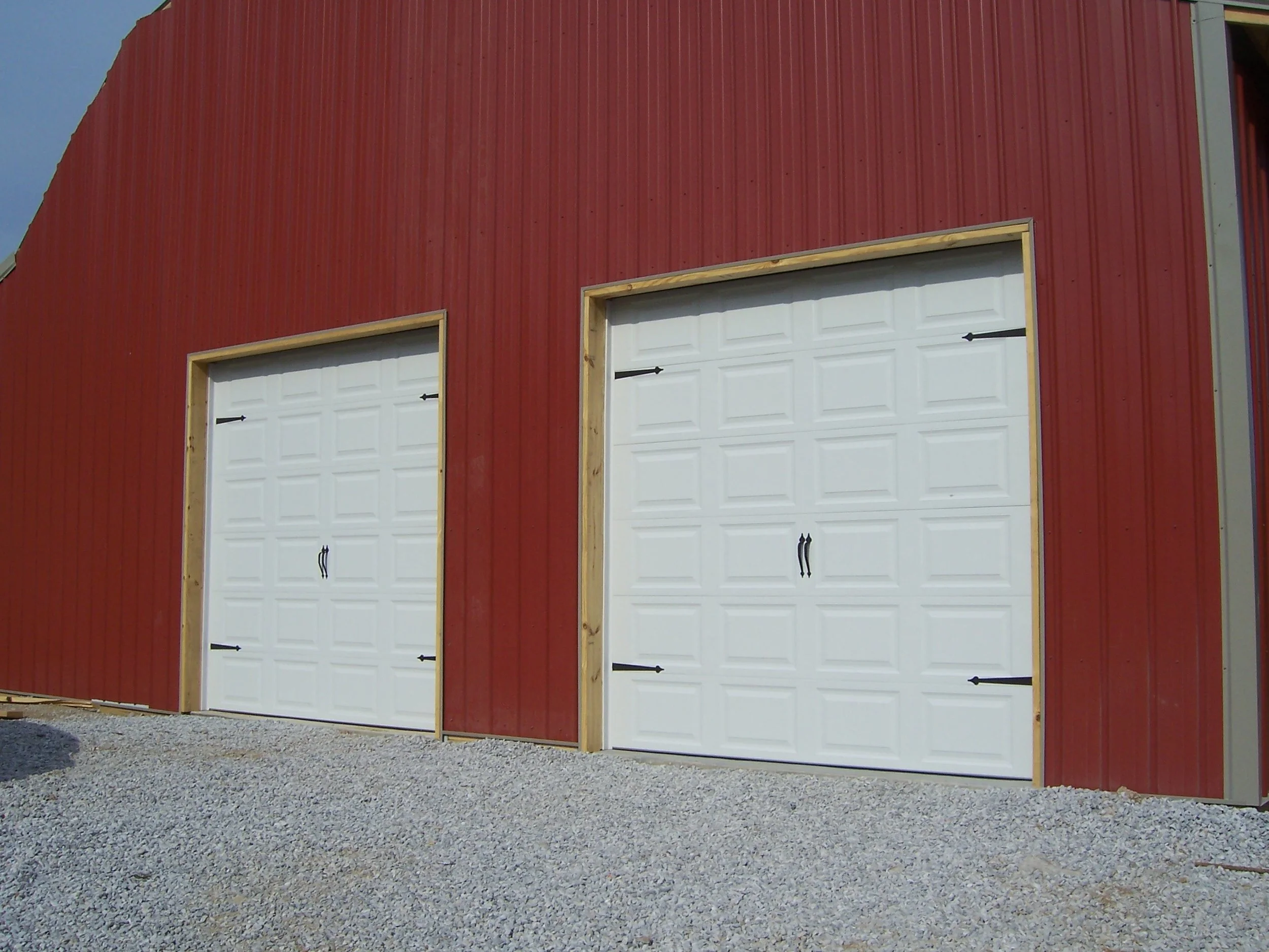 Red metal pole barn with two newly installed white sectional garage doors